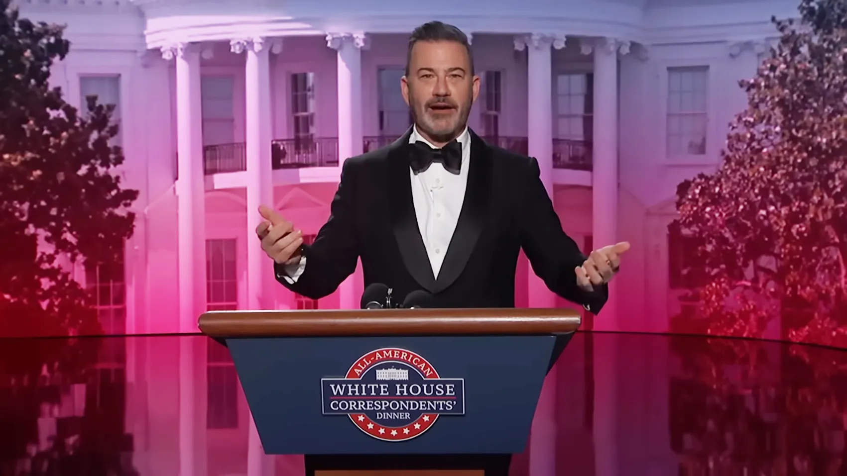 Jimmy Kimmel hosting the White House Correspondents' Dinner, wearing a tuxedo with the White House in the background.