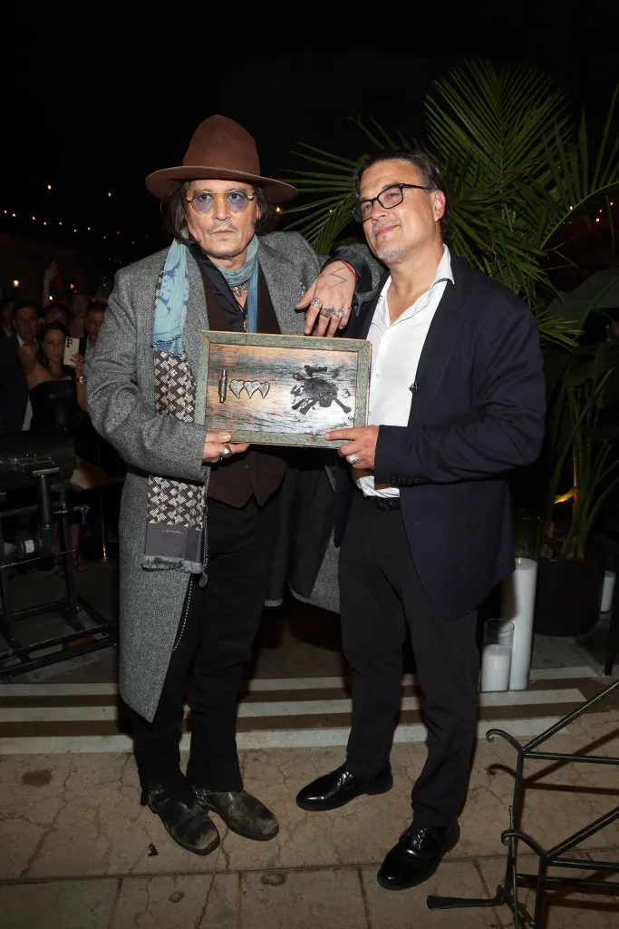 Johnny Depp and Bobby DeLeon holding a wooden plaque with the "Three Hearts" rum logo.