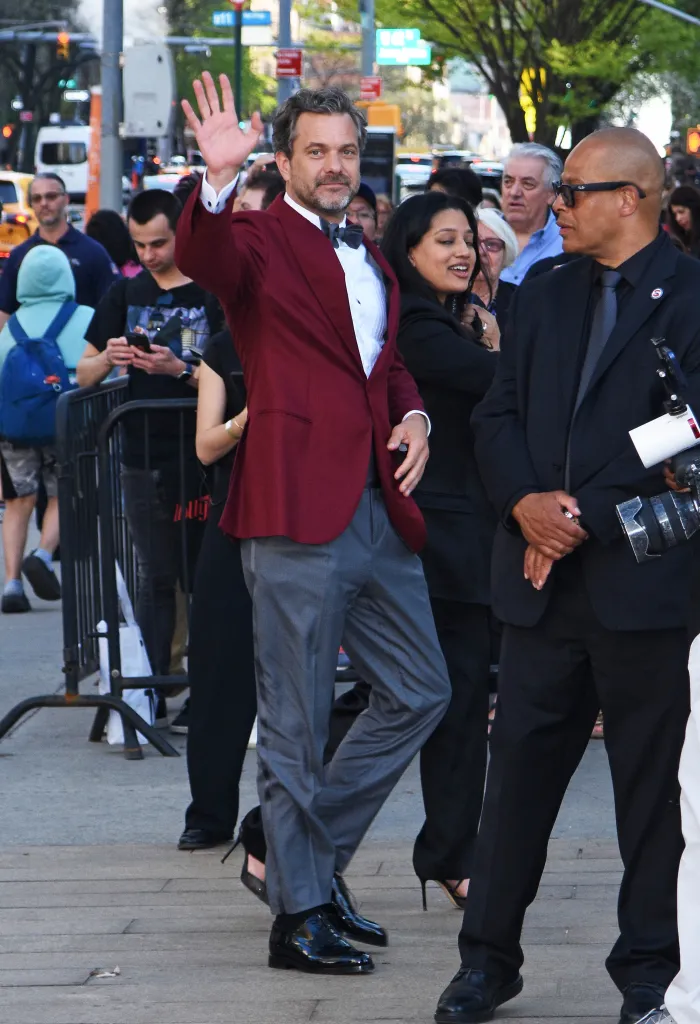 Joshua Jackson wearing a maroon tuxedo jacket, grey dress pants, and a dark grey bow tie.