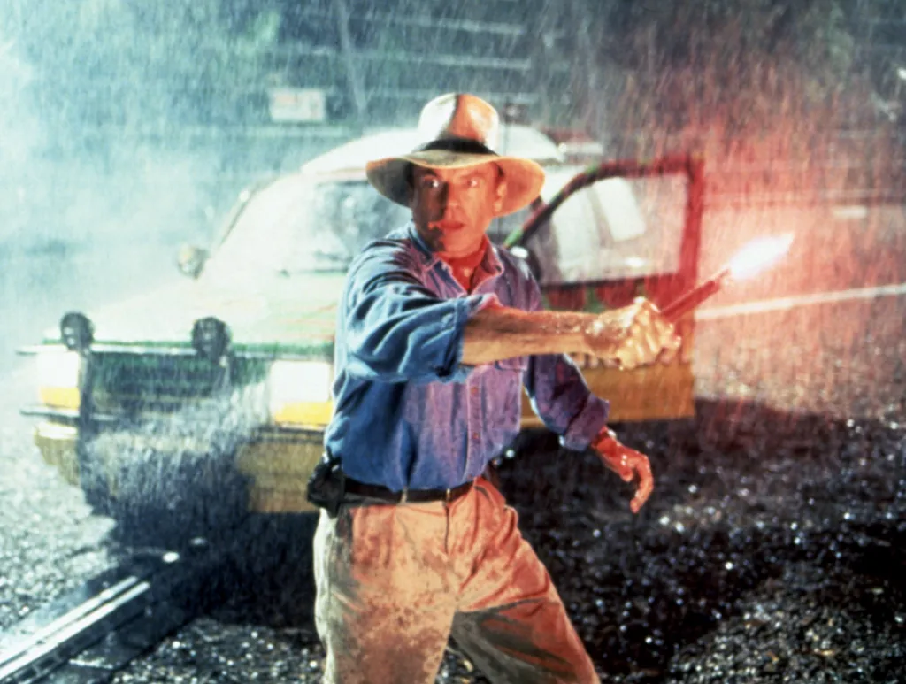 Sam Neill as Dr. Alan Grant in Jurassic Park, holding a flare in the rain.