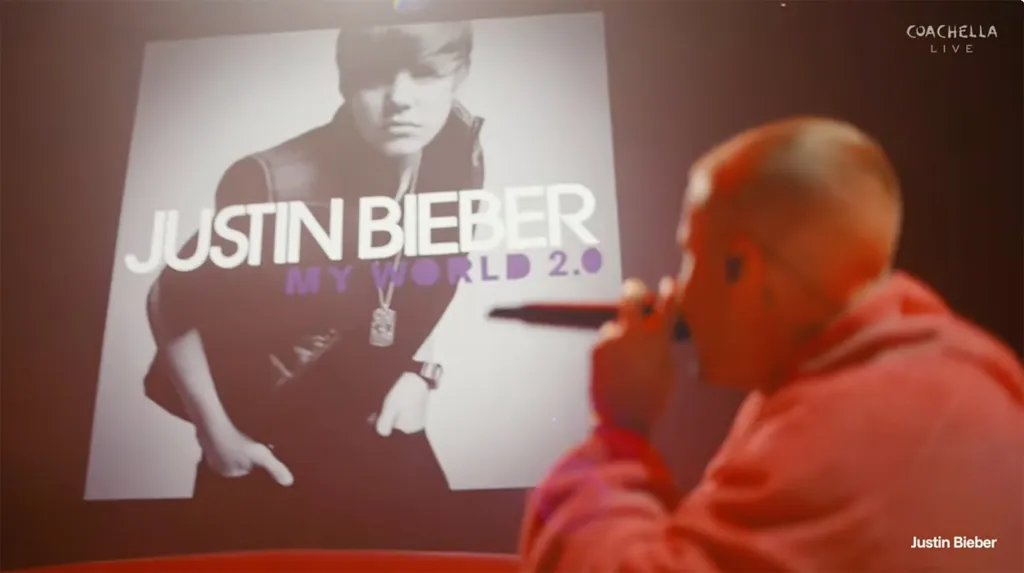 Justin Bieber performing at Coachella, with a large screen behind him displaying the cover art for his album "My World 2.0".