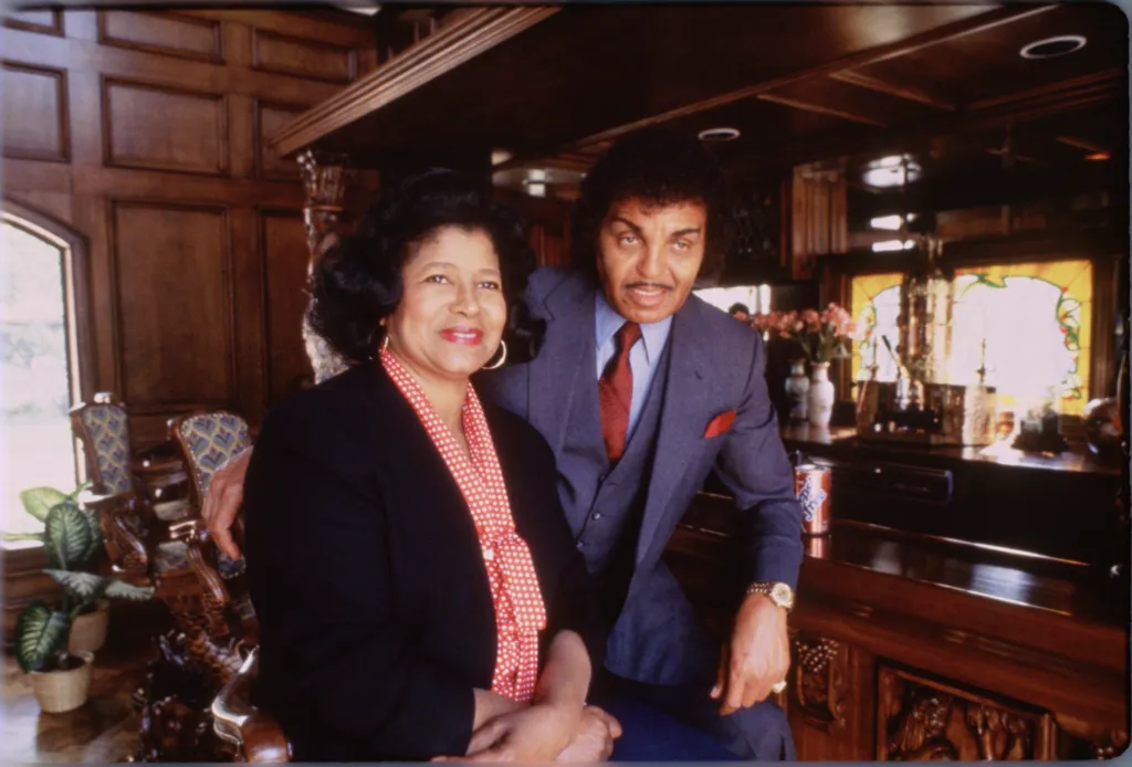 Katherine Jackson wearing a black jacket and red polka dot blouse with Joe Jackson in a gray suit and red tie.