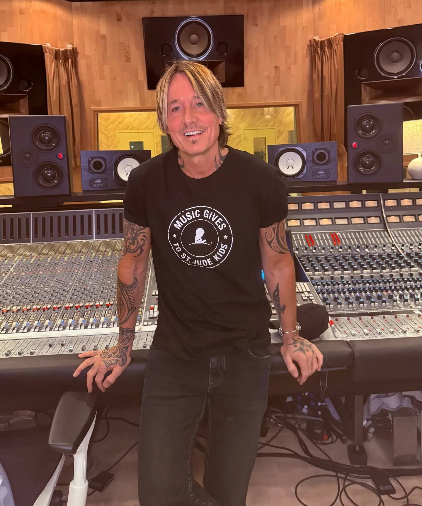 Keith Urban smiling in a recording studio, wearing a "Music Gives To St. Jude Kids" t-shirt.