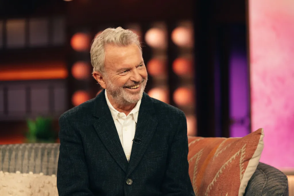 Sam Neill smiling during an interview on The Kelly Clarkson Show.