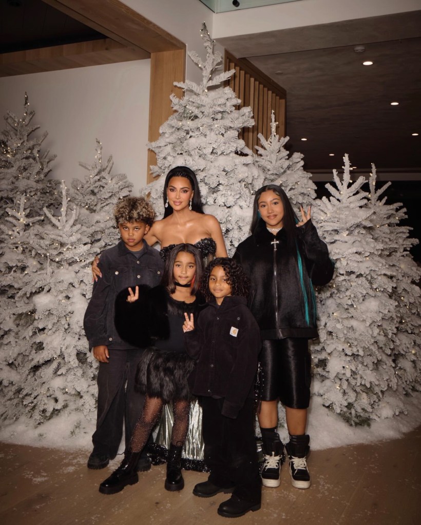 Kim Kardashian with her children and nieces/nephews posing in front of snowy Christmas trees.