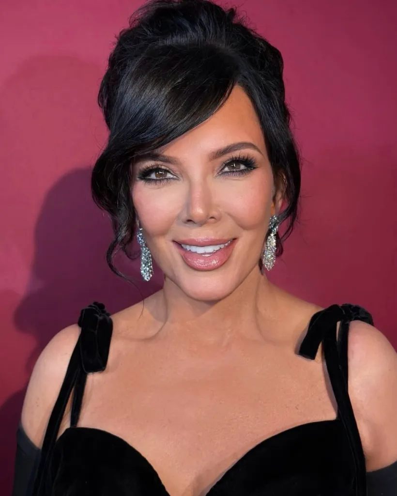 Kris Jenner smiling at the camera, wearing a black dress and sparkly earrings.