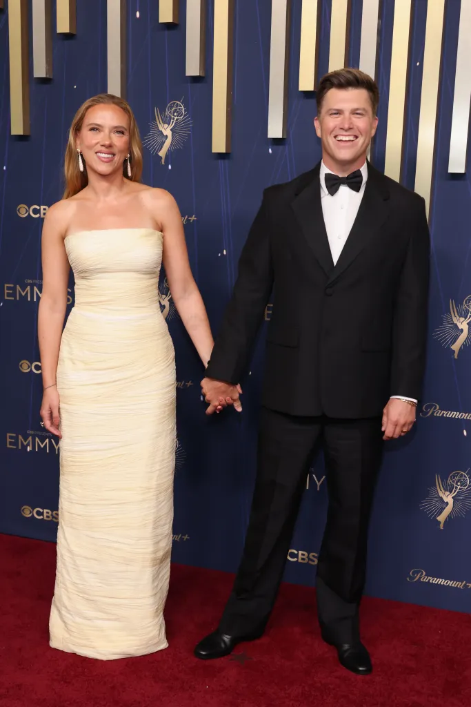 Scarlett Johansson in a light yellow strapless dress holding hands with Colin Jost in a black tuxedo at the 77th Primetime Emmy Awards.
