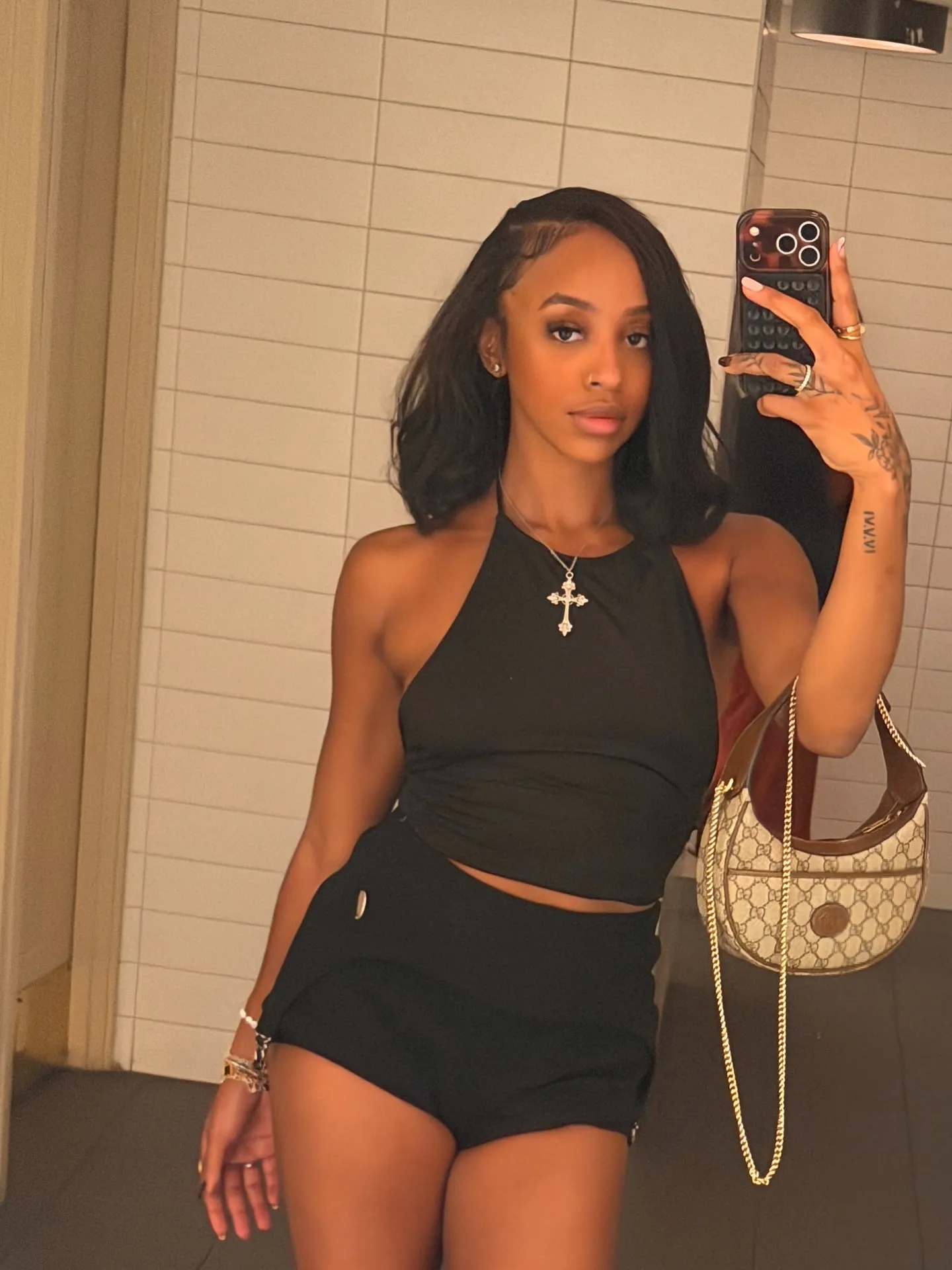 Lexie Brown in a mirror selfie wearing a black halter top and black shorts, holding a small purse.