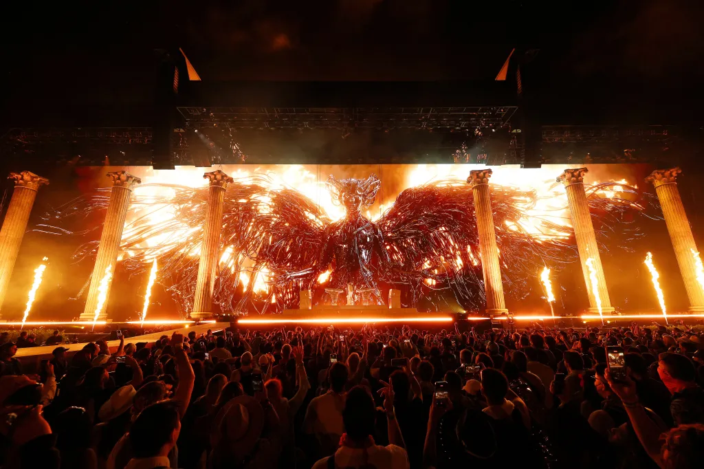 Anyma performs at Coachella, with a large flaming Phoenix-like visual on stage flanked by Roman-style columns and pyrotechnics, as a large crowd watches.