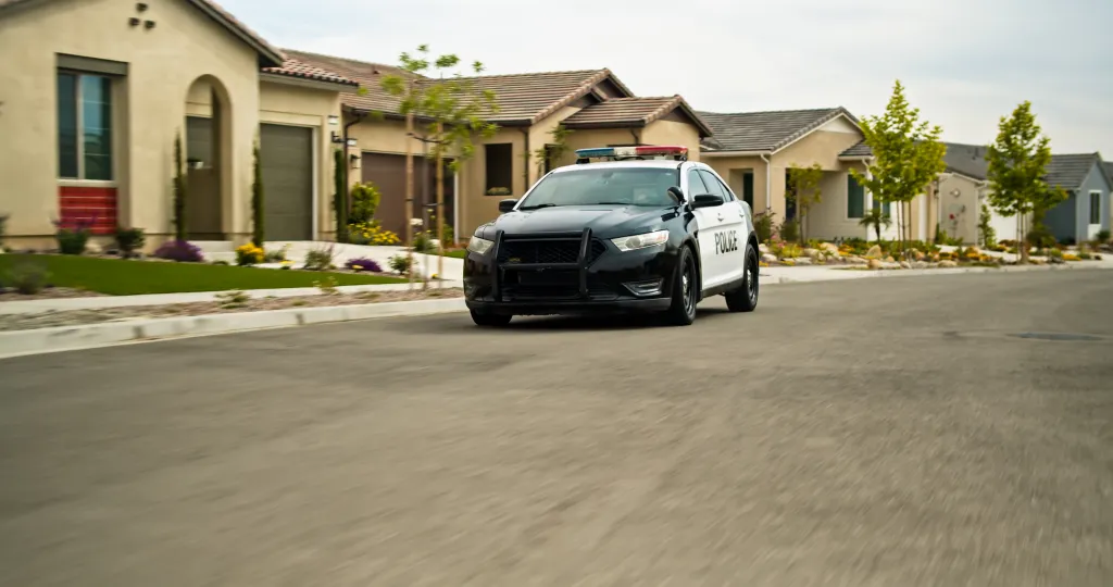 A police car driving down a residential street in a Californian suburb.