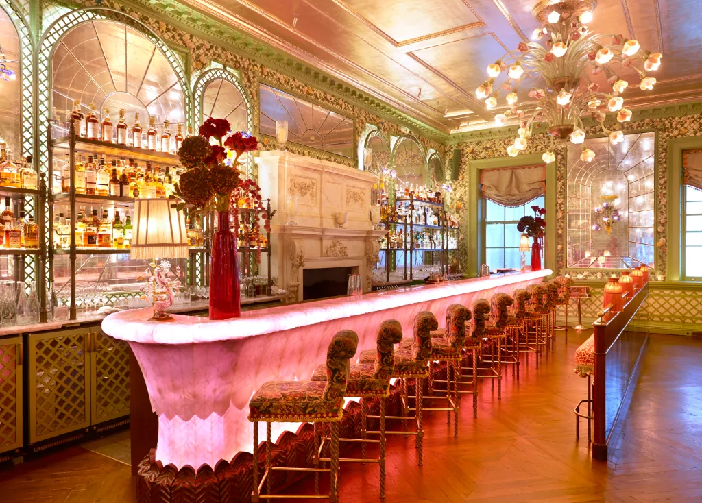 The Rose Room Bar at Annabel's Nightclub, featuring a long, illuminated bar with floral stools, a fireplace, and a mirrored, arched window design.
