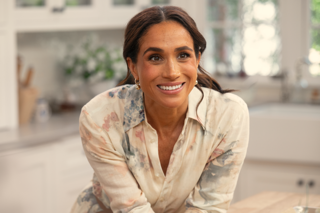 Meghan, Duchess of Sussex, smiles at the camera in a kitchen setting.