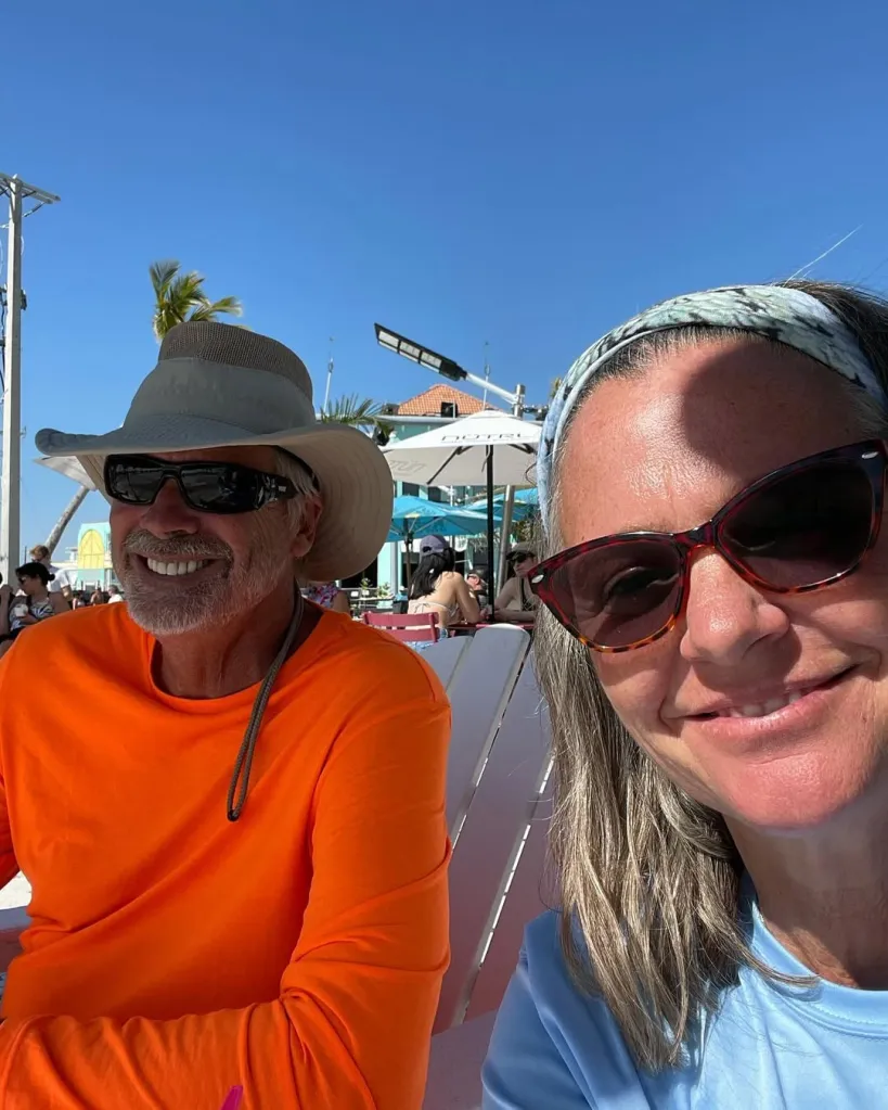 Lynette Hooker, 55, and husband Brian, 58, smiling while sitting outdoors on a sunny day.