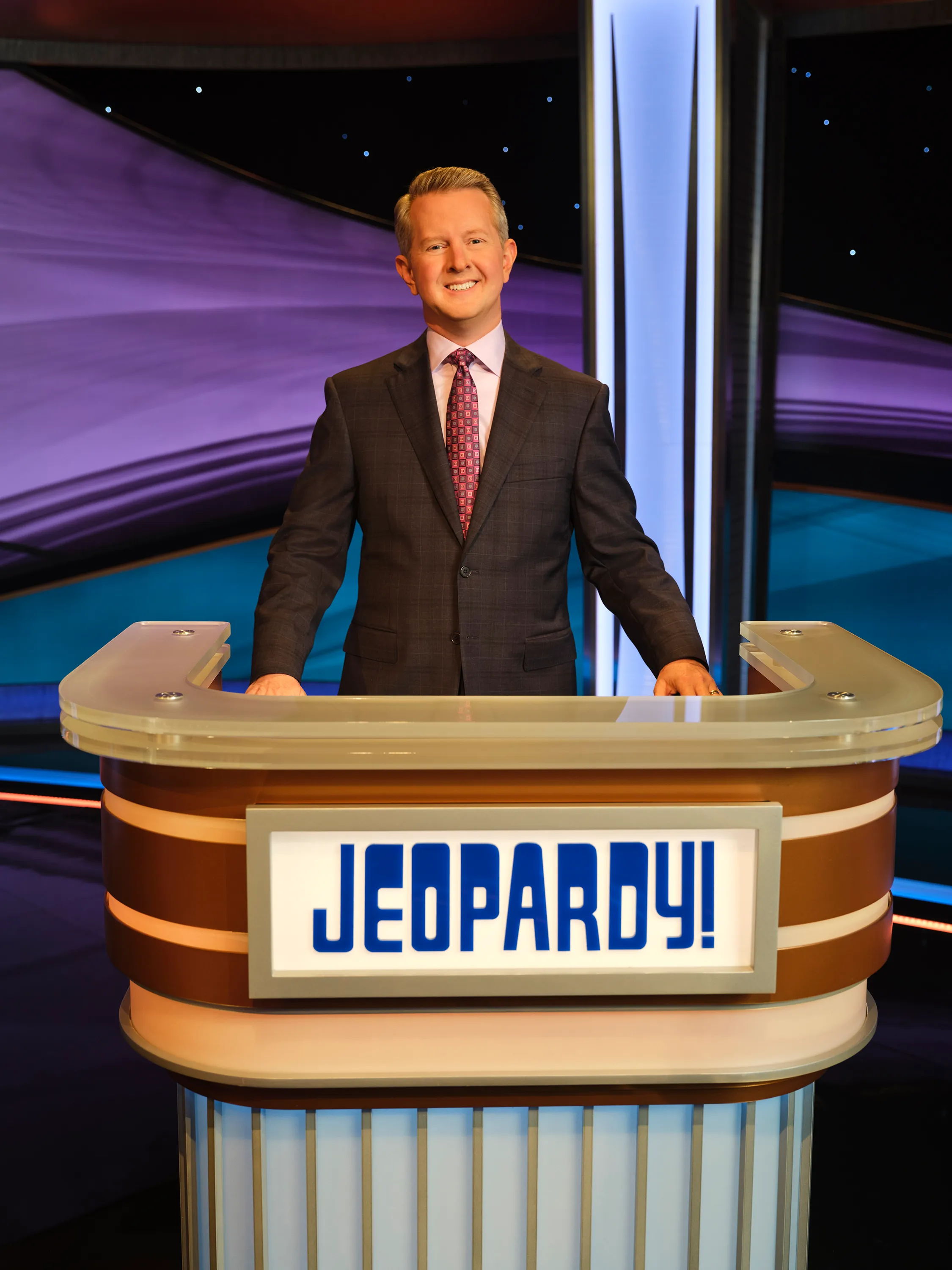 Ken Jennings smiling behind the Jeopardy! host's podium.