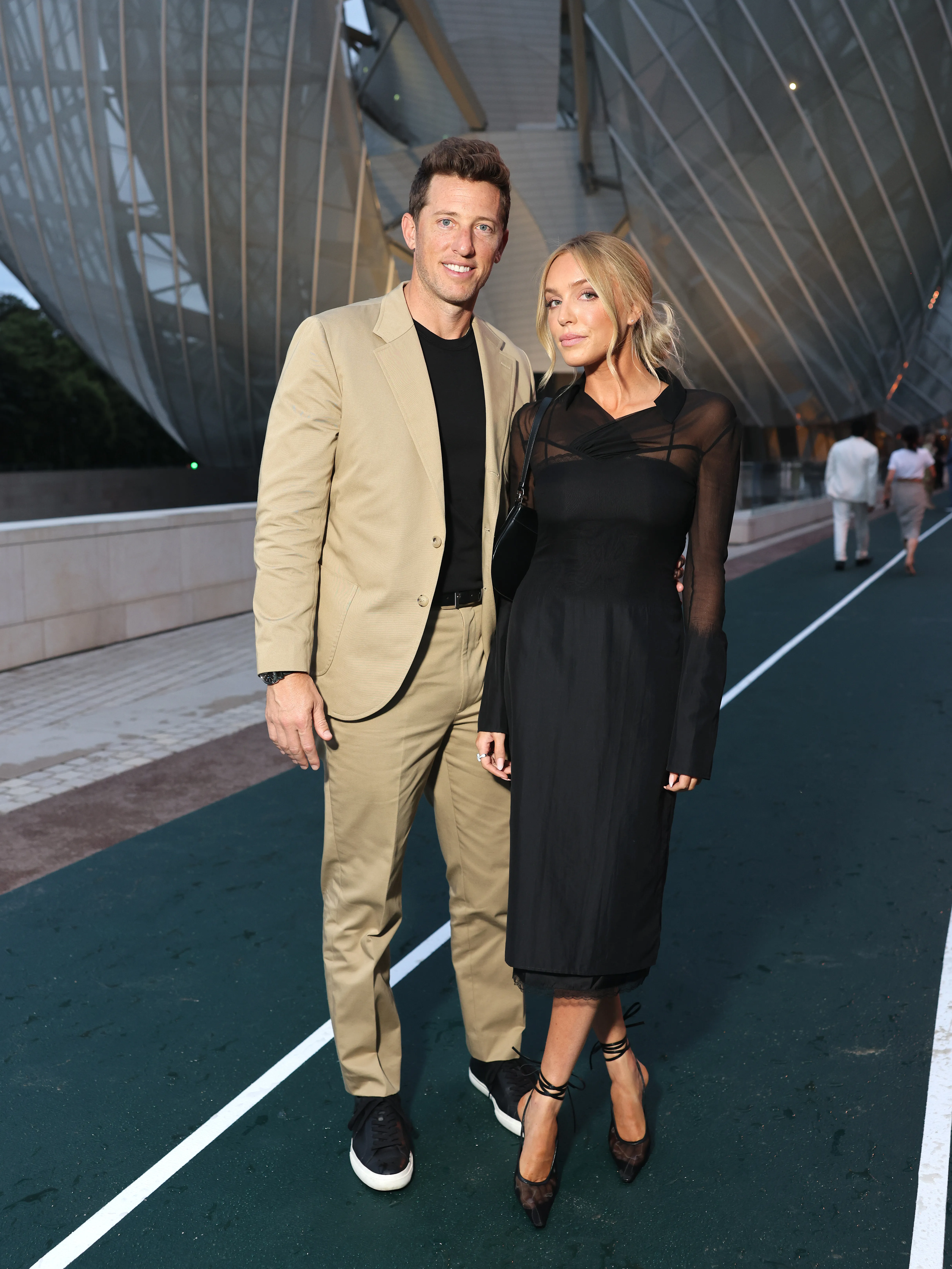 Matt Kaplan and Alex Cooper pose together on a green track in front of the Fondation Louis Vuitton.