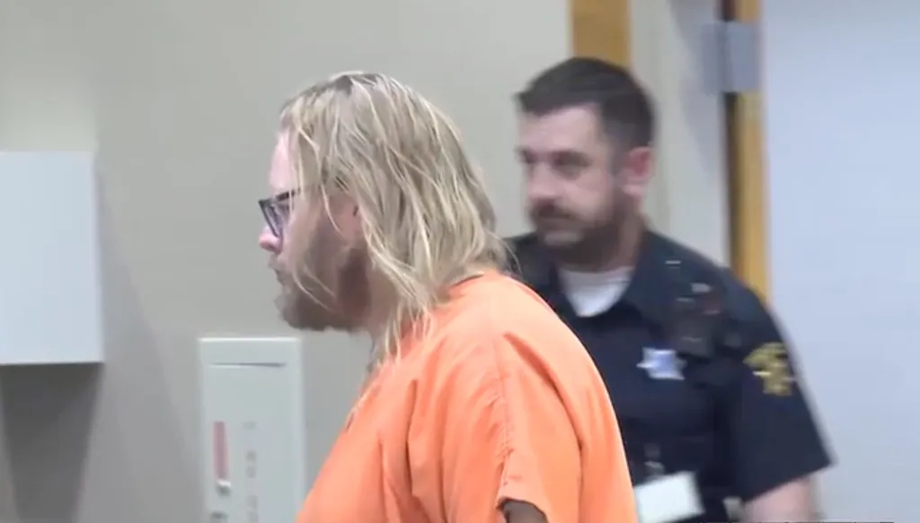 Matthew Lund in an orange jumpsuit is escorted by an officer.