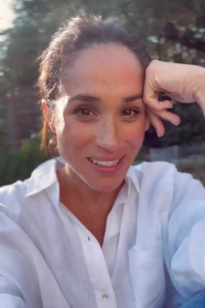 Meghan Markle smiling with her hand resting on her forehead.