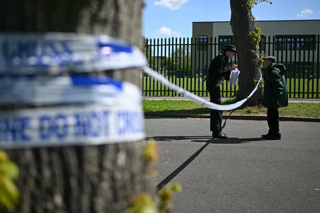 A police officer speaks to a man behind a "POLICE DO NOT CROSS" cordon.