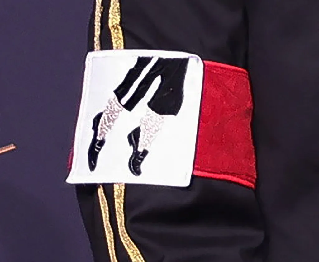 A black sleeve with gold stripes and a white and red armband featuring an illustration of Michael Jackson's legs doing the moonwalk.
