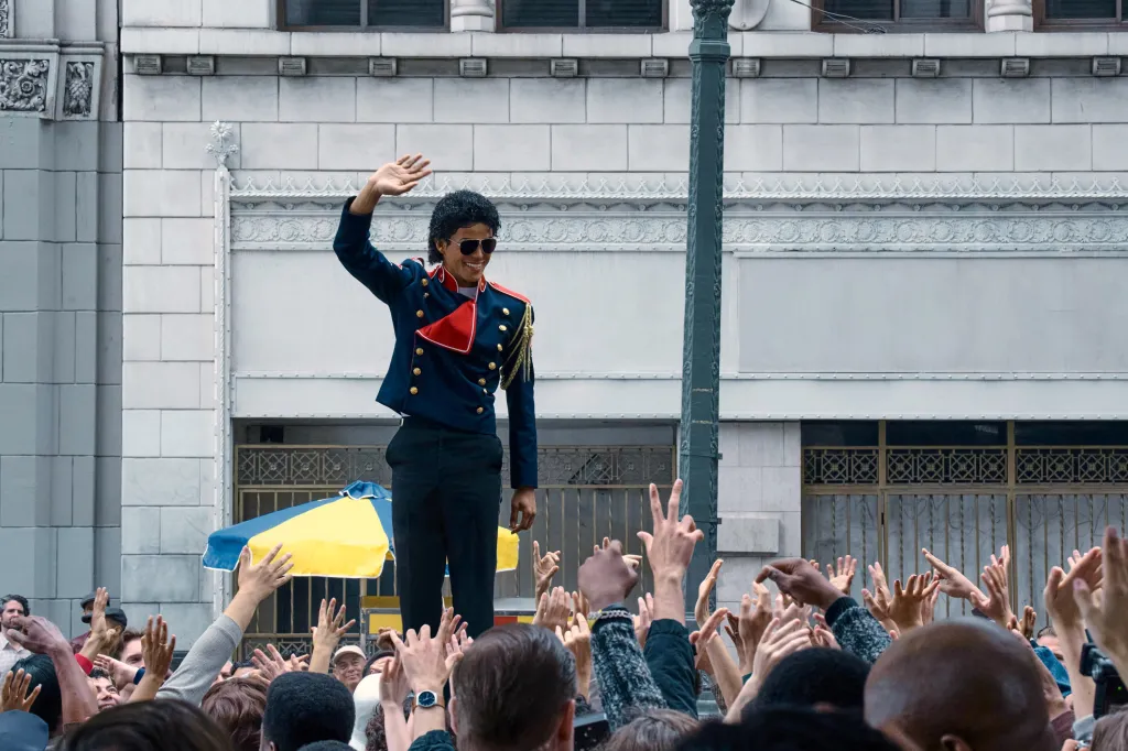 Jaafar Jackson as Michael Jackson, waving to a crowd in a military-style jacket and sunglasses.