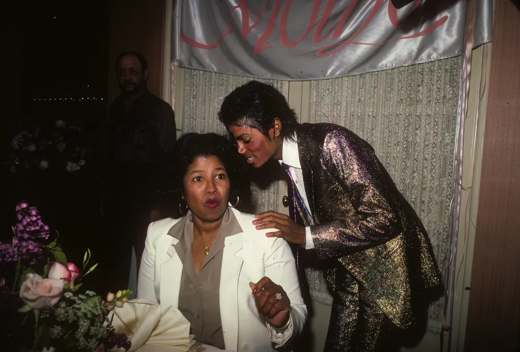 Michael Jackson in a shimmering suit speaks to his mother, Katherine Jackson, in a white blazer.