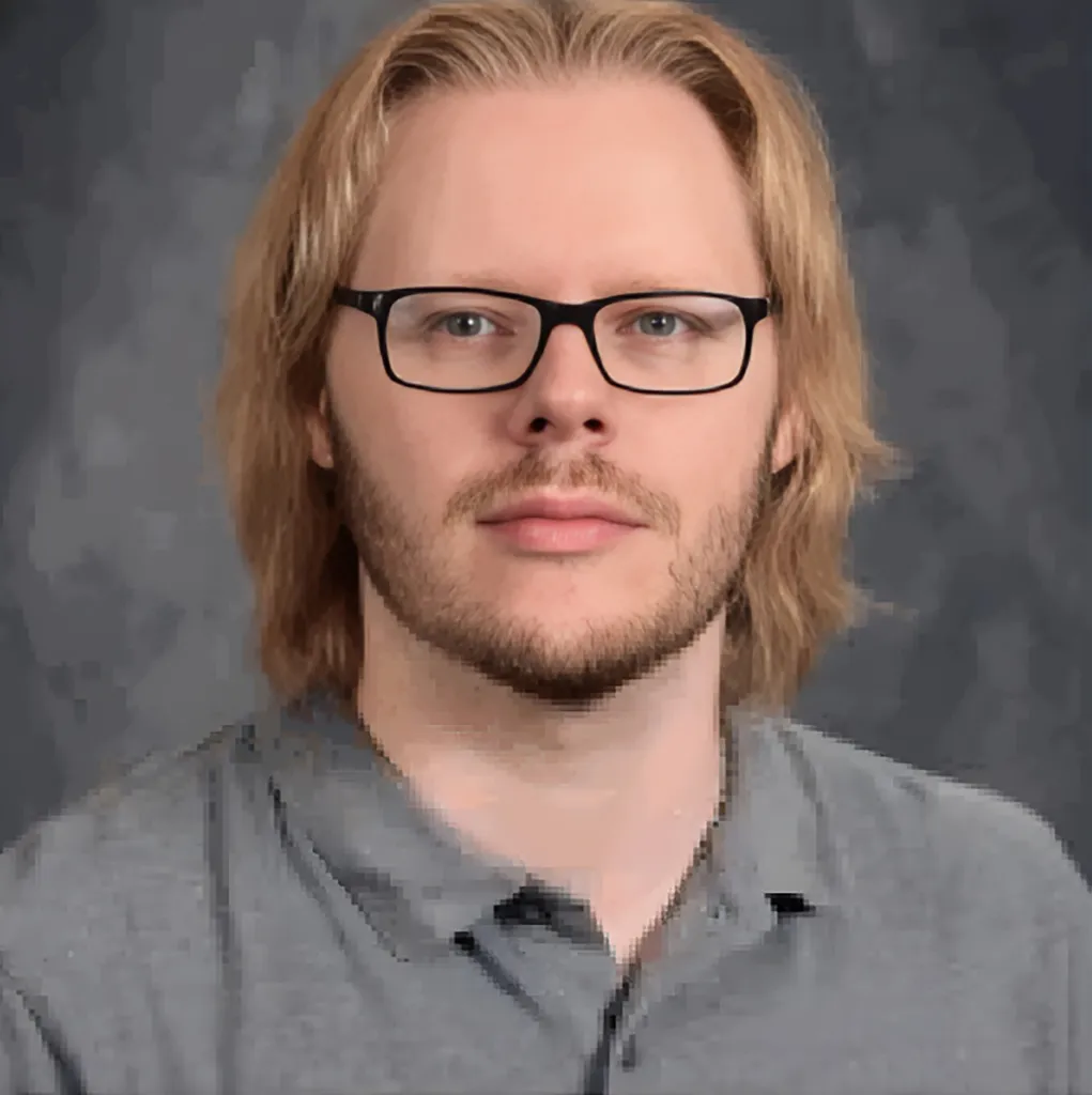 Matthew Lund, a man with blond hair, glasses, and a beard, wearing a gray polo shirt.