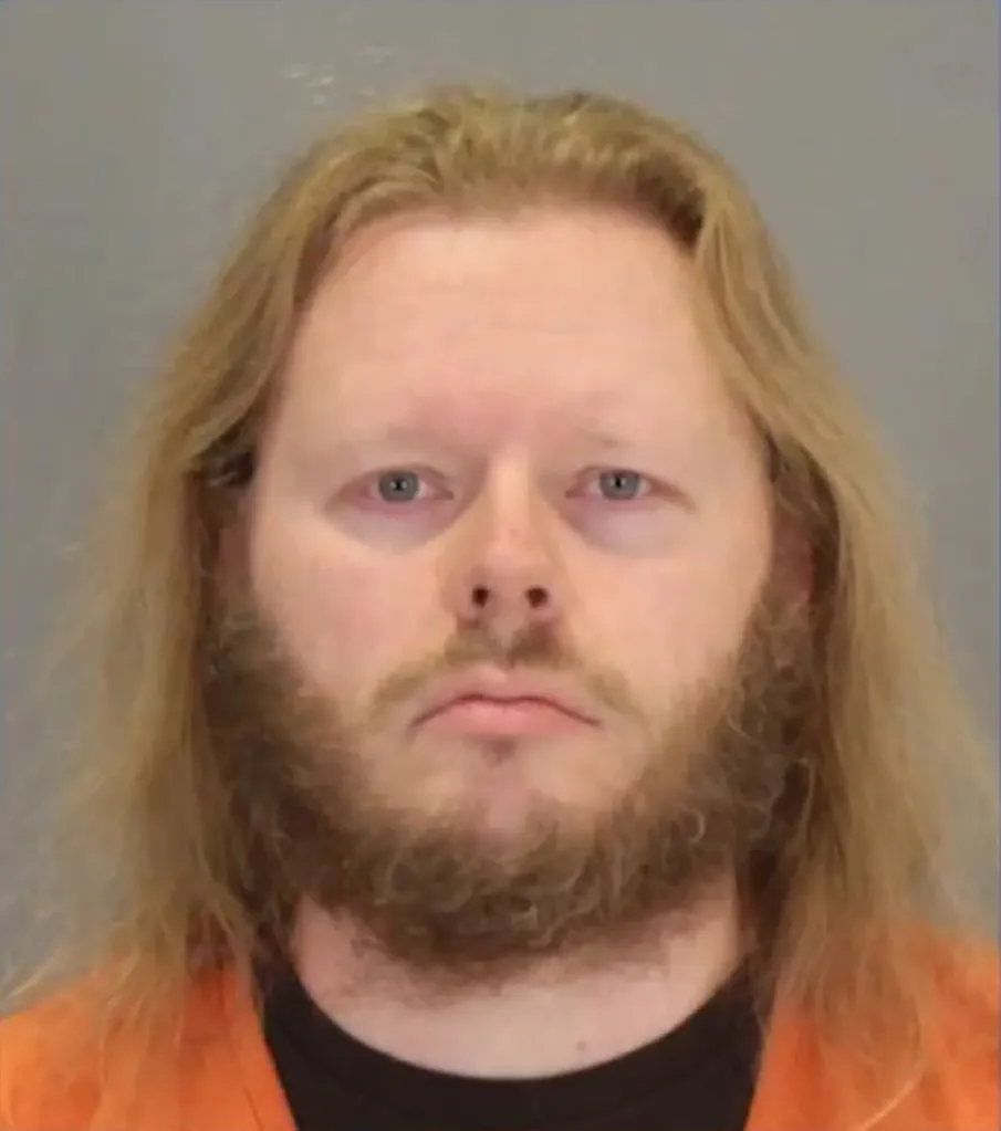 Mugshot of Matthew Lund, a white man with long blond hair and a beard, wearing an orange jumpsuit.