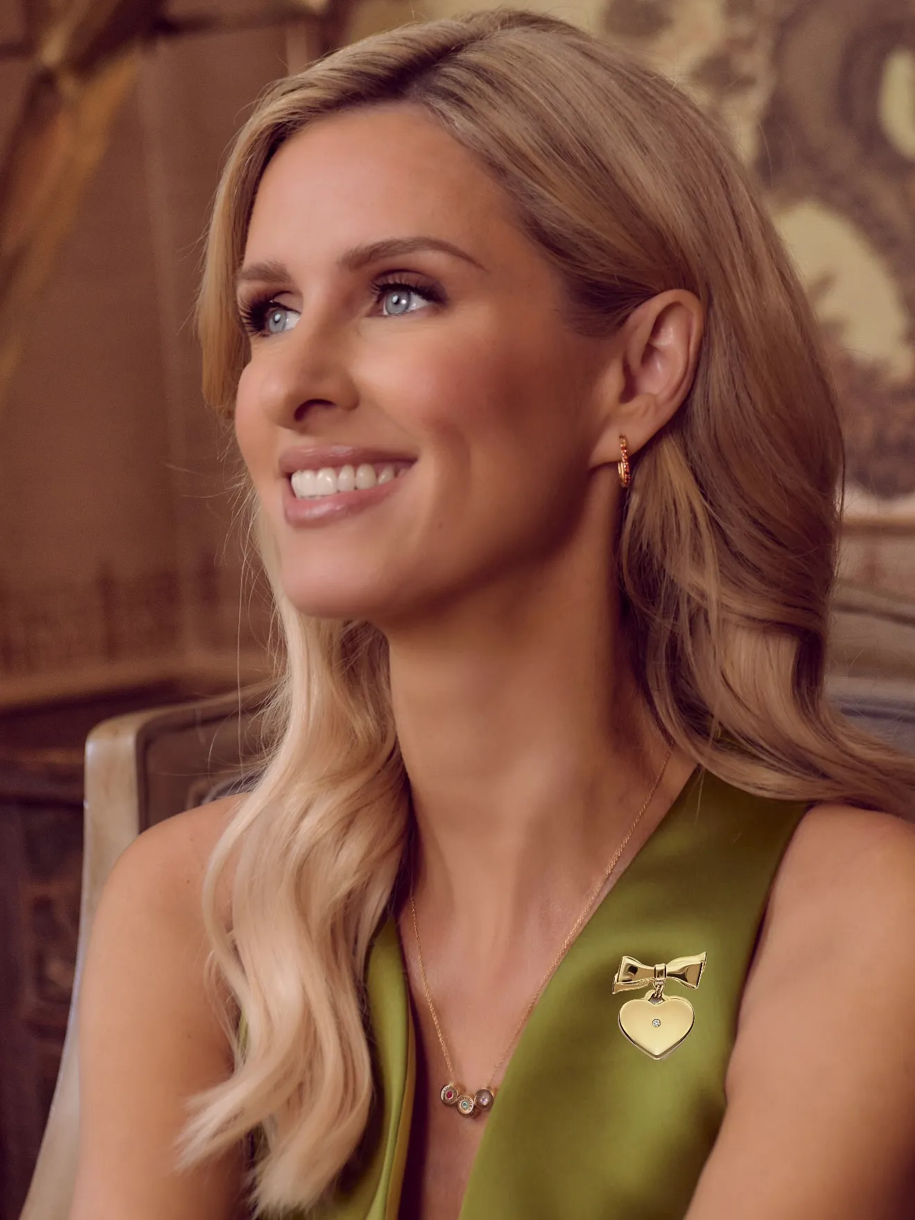Nicky Hilton wearing a gold heart brooch with a bow and diamond on an olive green dress.