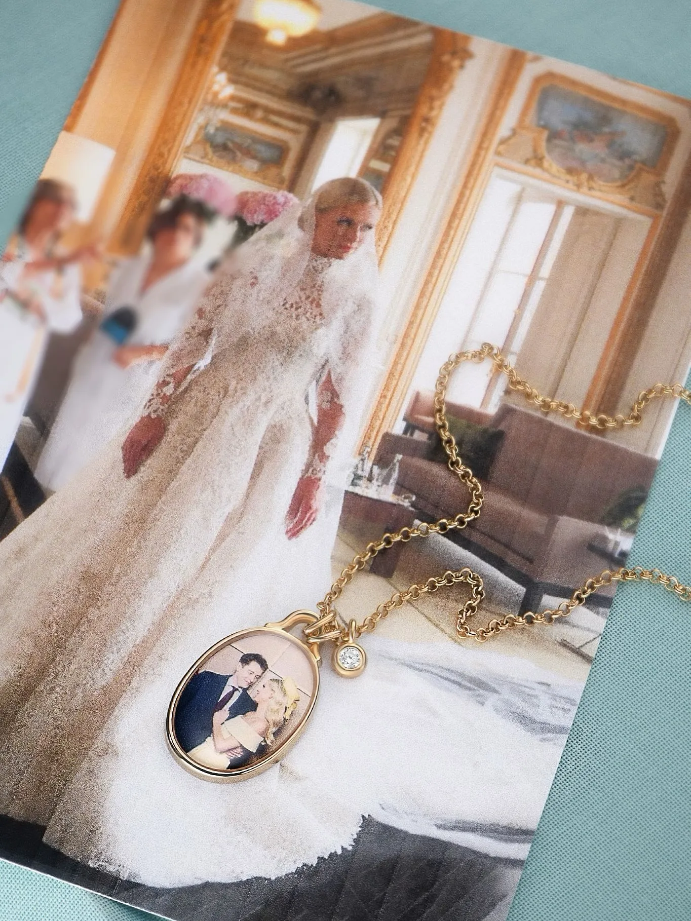 A gold locket featuring a photo of a couple, with a small diamond charm, resting on a picture of a bride in a long white dress.