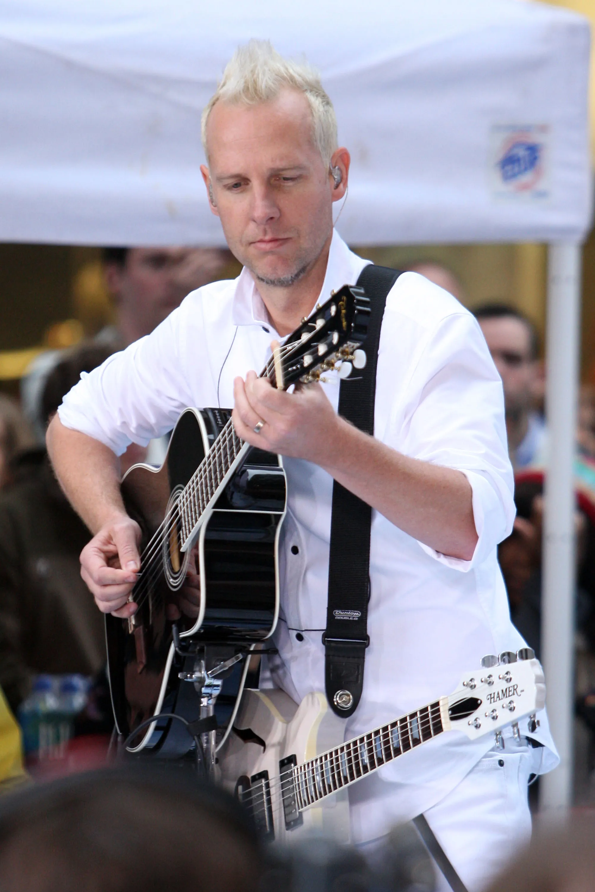Tom Dumont of No Doubt playing an acoustic guitar and wearing a white shirt.