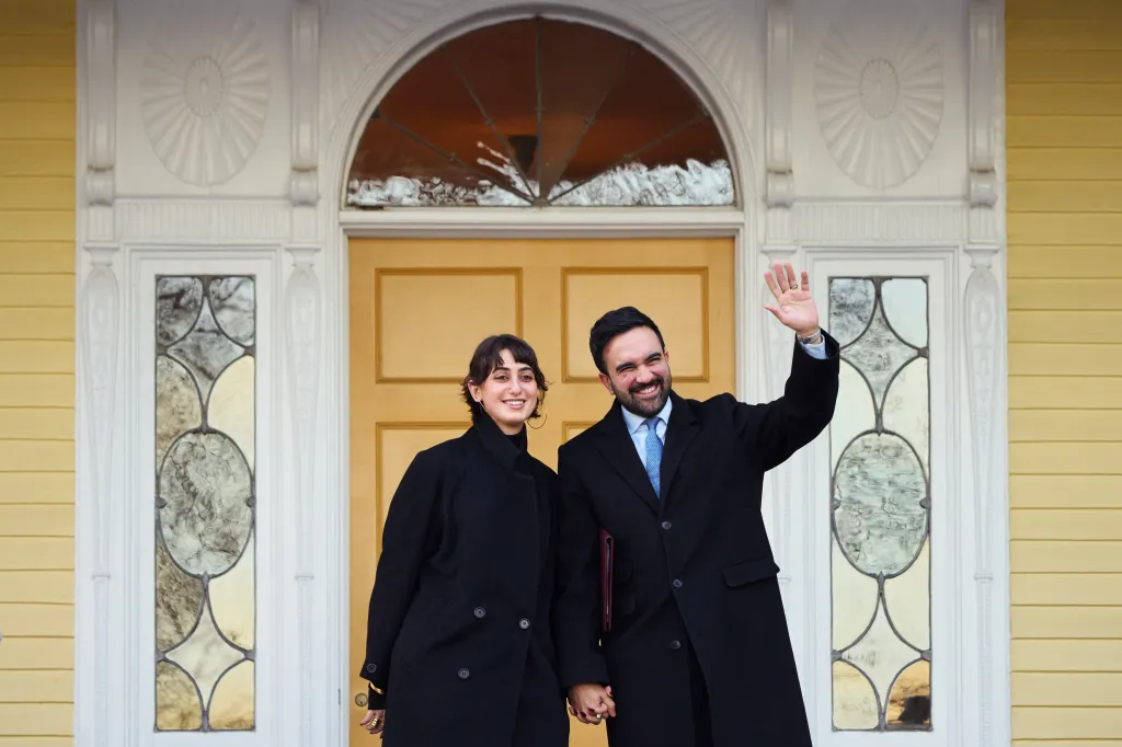Mayor Zohran Mamdani and his wife, First Lady Rama Duwaji, wave from the entrance of Gracie Mansion.