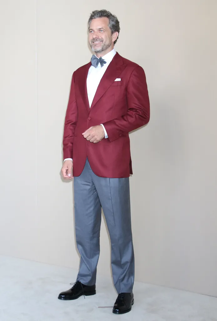 Joshua Jackson wearing a maroon tuxedo jacket, grey dress pants, and a dark grey bow tie.