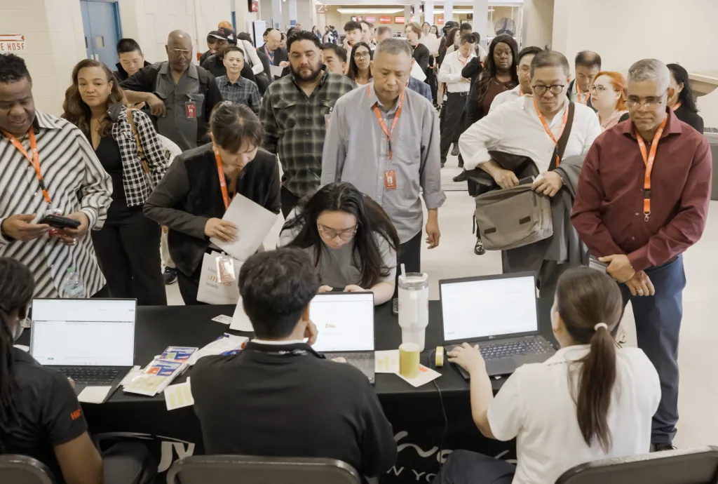 People waiting in a line for an event while staff members sit behind a table with laptops.