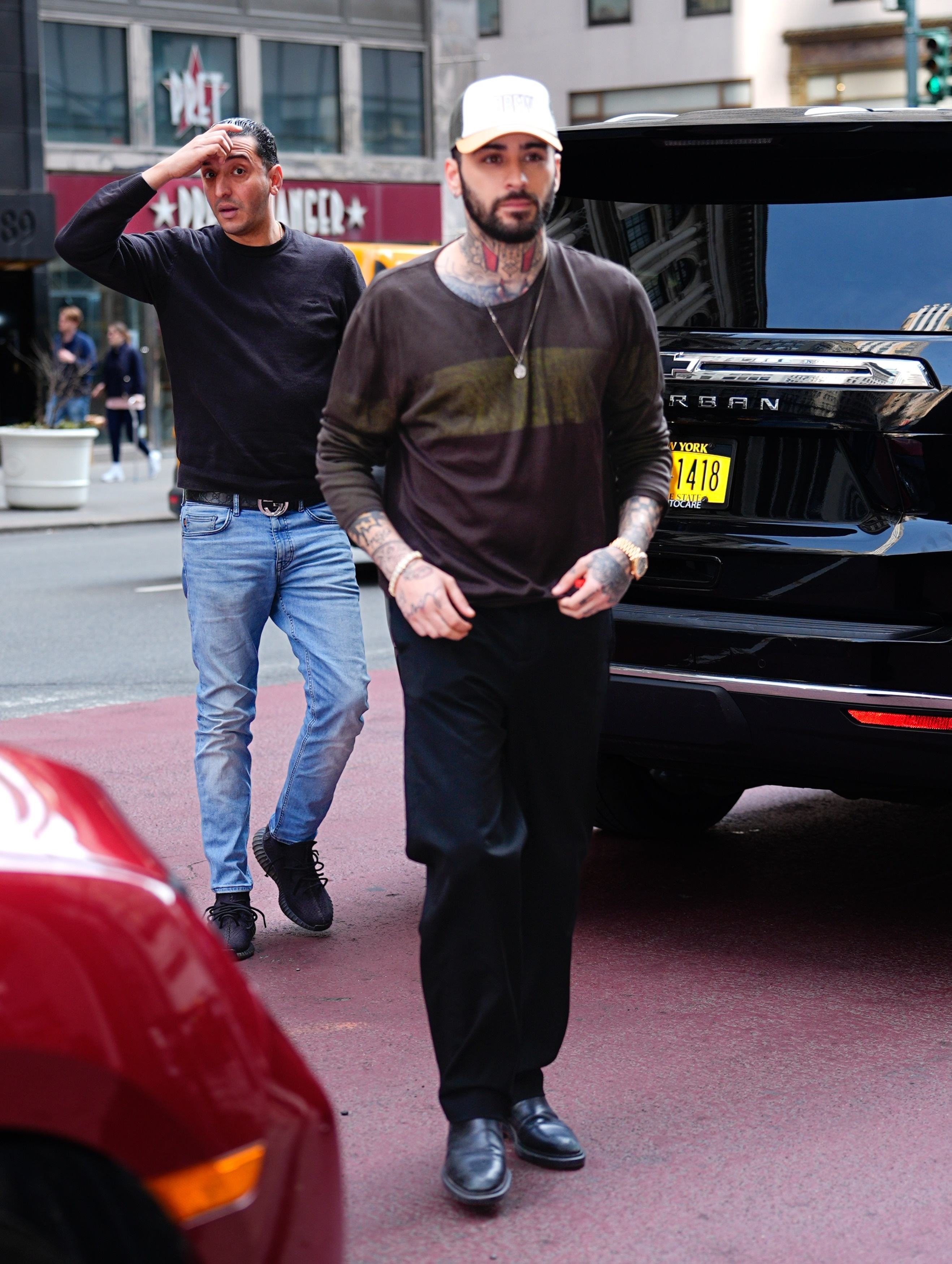 Zayn Malik arriving at a New York City hotel wearing a brown sweater, black trousers, and a white cap.