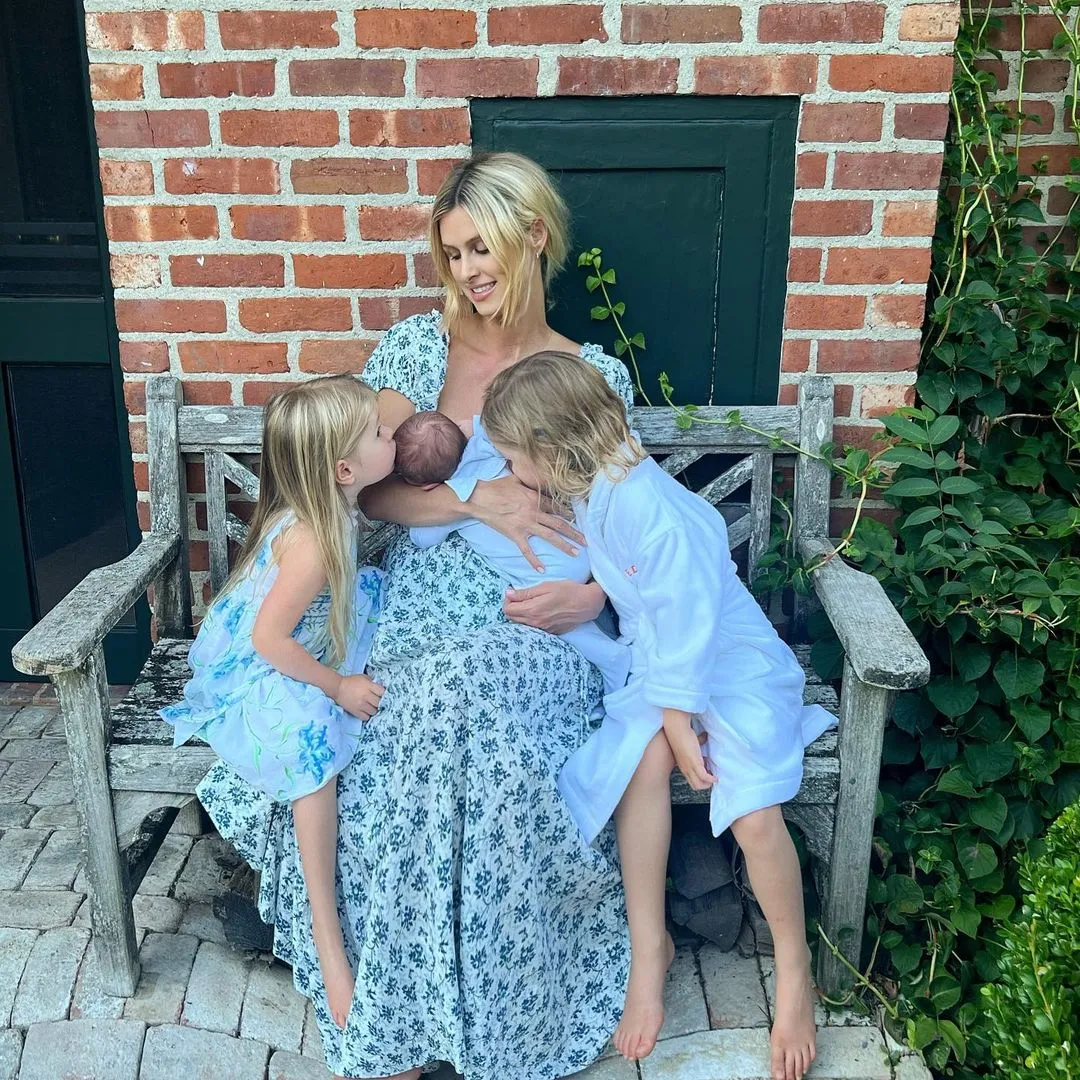 Nicky Hilton holding her newborn baby as her two daughters, Lily-Grace and Theodora, lean in to kiss the baby.