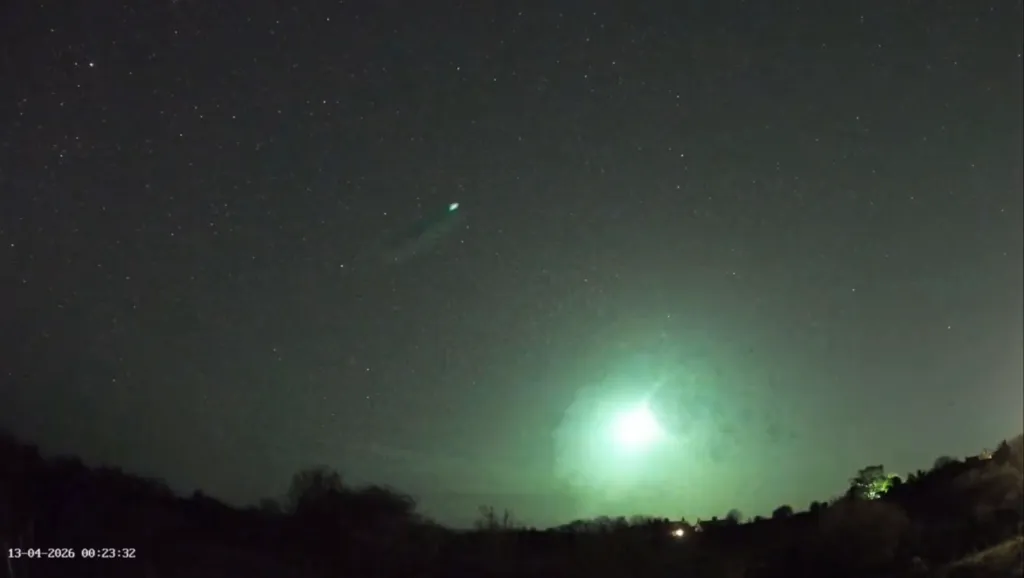 A bright green fireball streaks across the night sky, illuminating the landscape below.