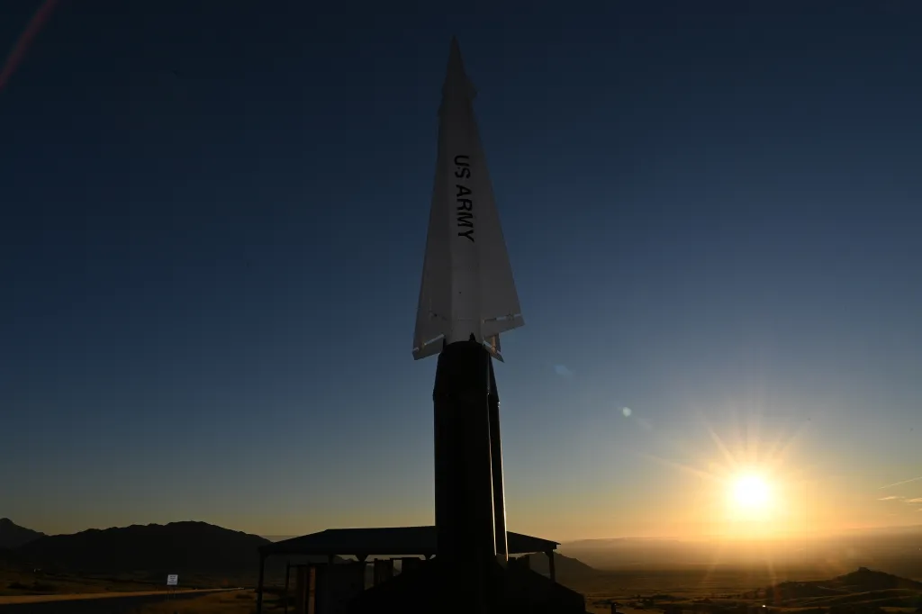 A missile with "US ARMY" printed on its side stands silhouetted against a setting sun over White Sands Missile Range.