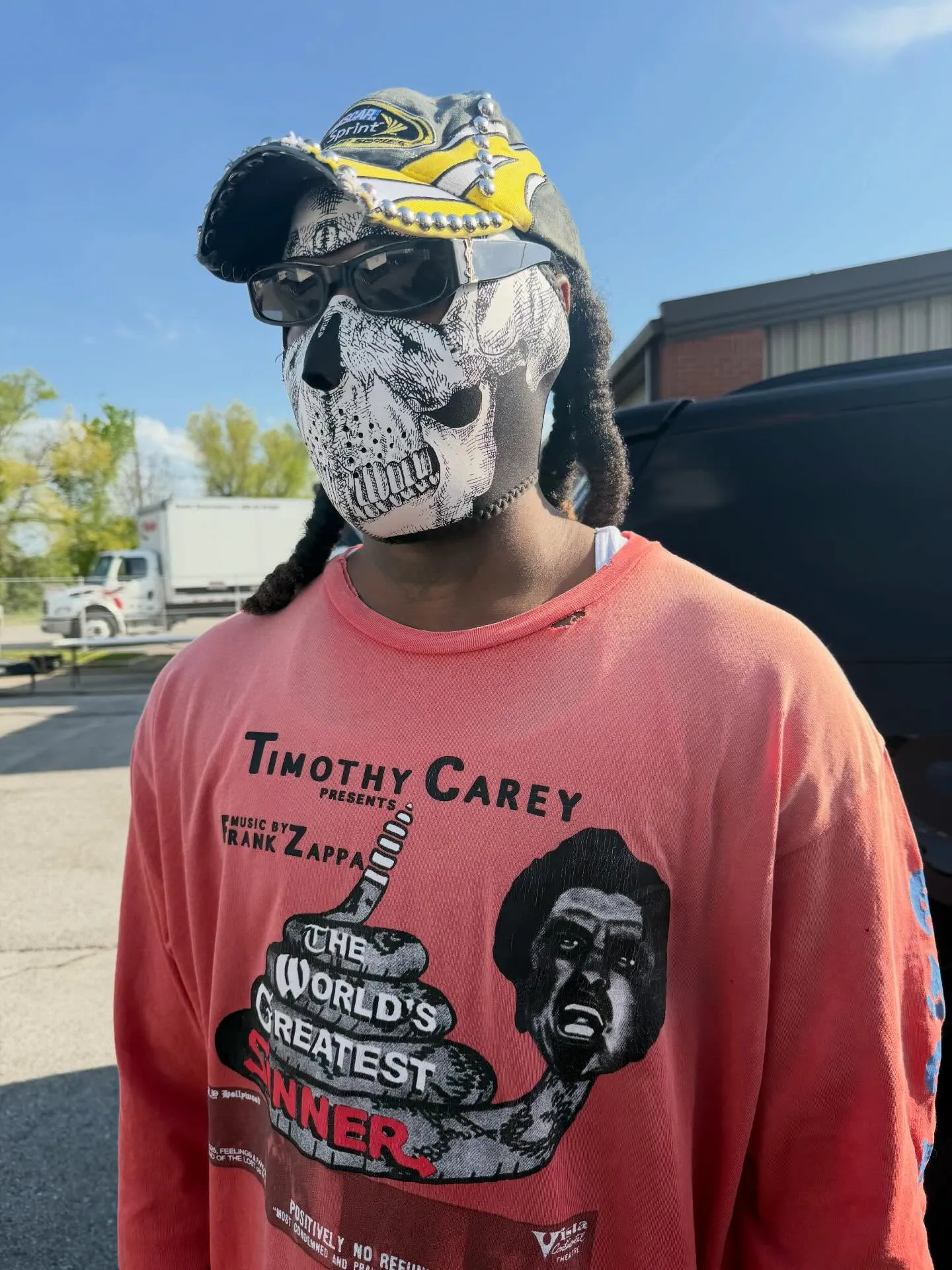 Offset wearing a skull mask, sunglasses, a baseball cap, and a "Timothy Carey Presents" long-sleeve shirt with a graphic of a snake and a face.