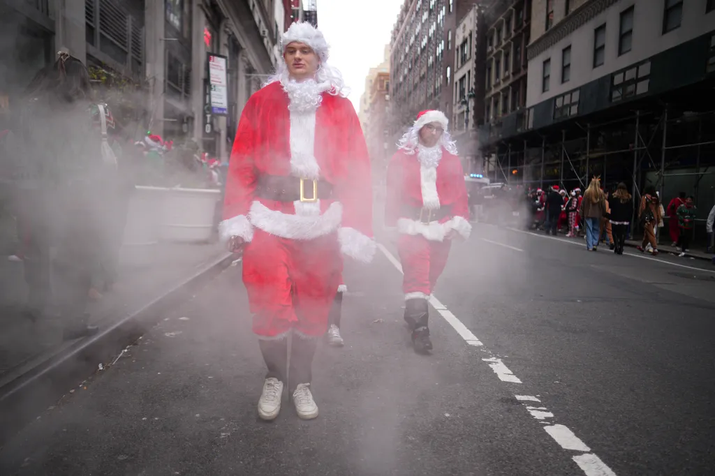Two men in Santa Claus costumes walking in the street with steam rising around them.