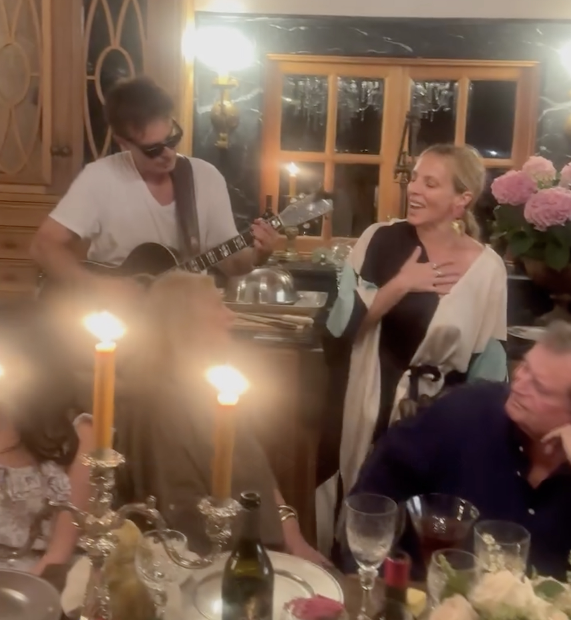Patrick Muldoon playing guitar and singing with a woman at a dinner table.