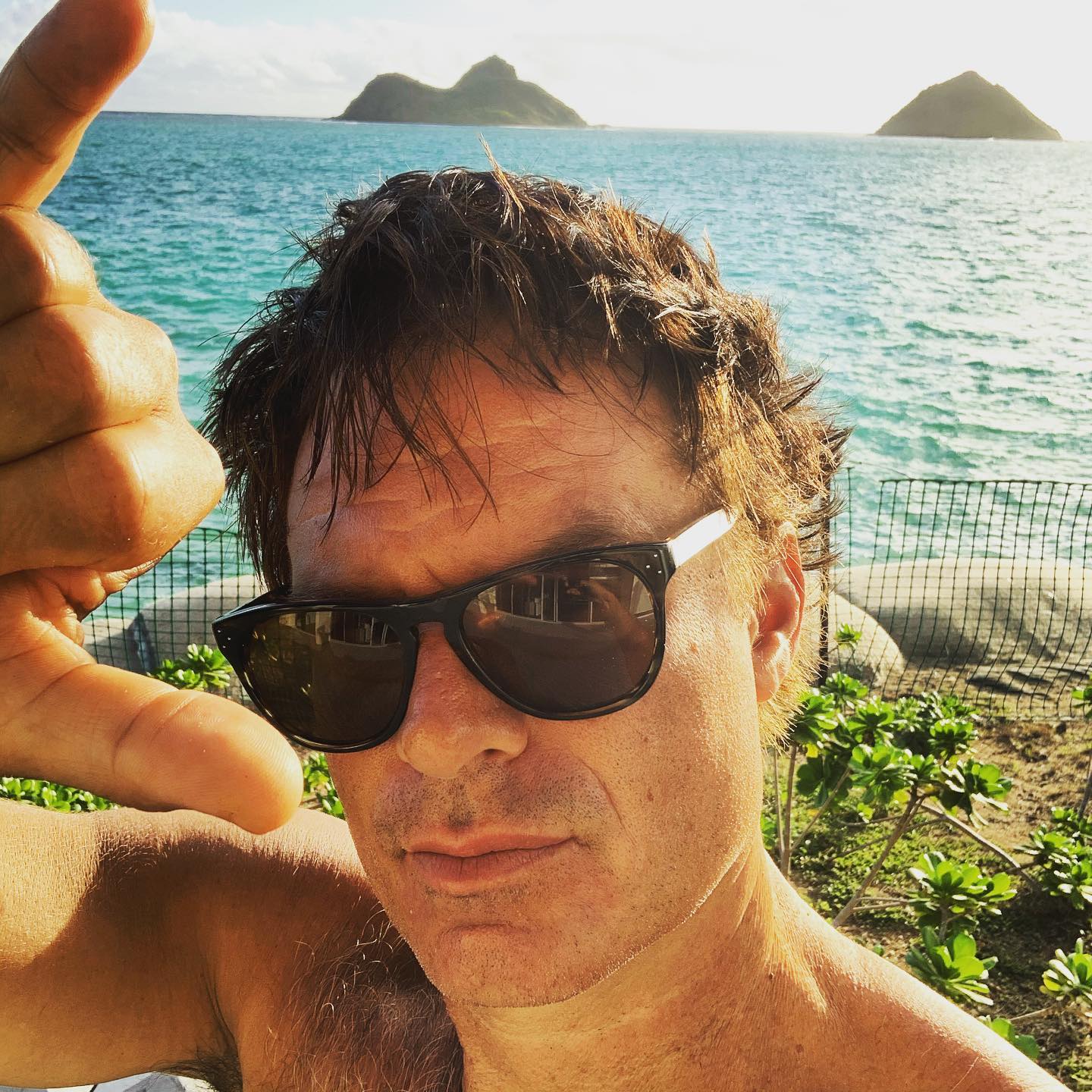 Patrick Muldoon wearing sunglasses and making a hand gesture with islands in the background.