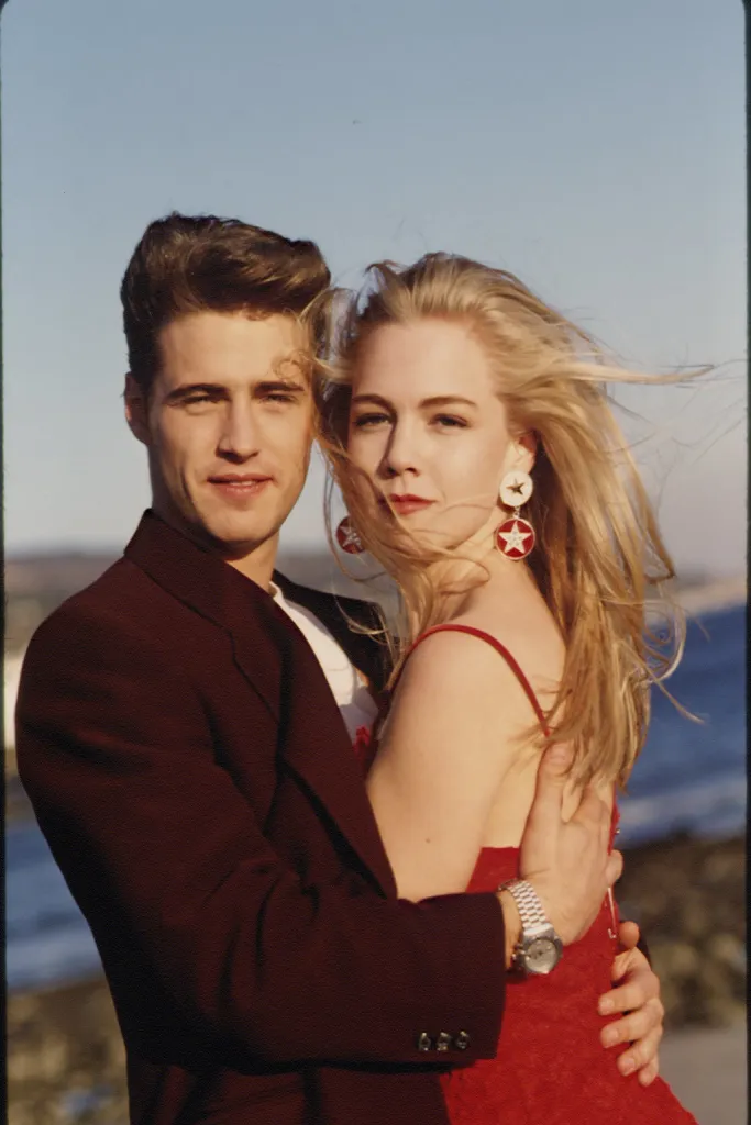 Jennie Garth and Jason Priestley smiling, dressed up and embracing.