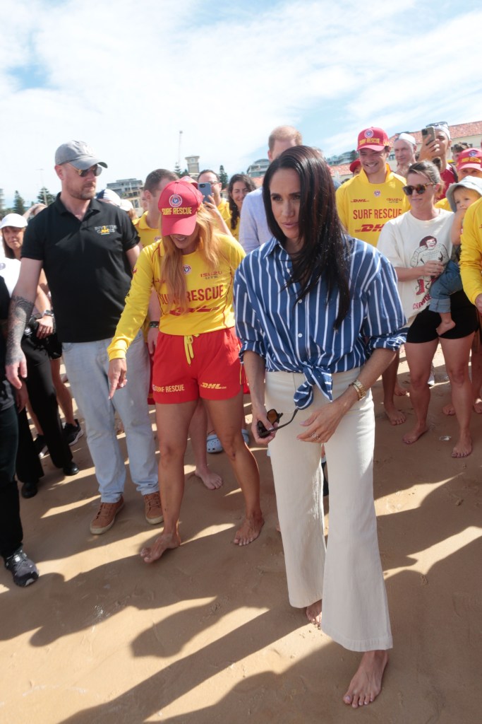 Prince Harry and Meghan Markle barefoot on Bondi Beach with surf rescue members.
