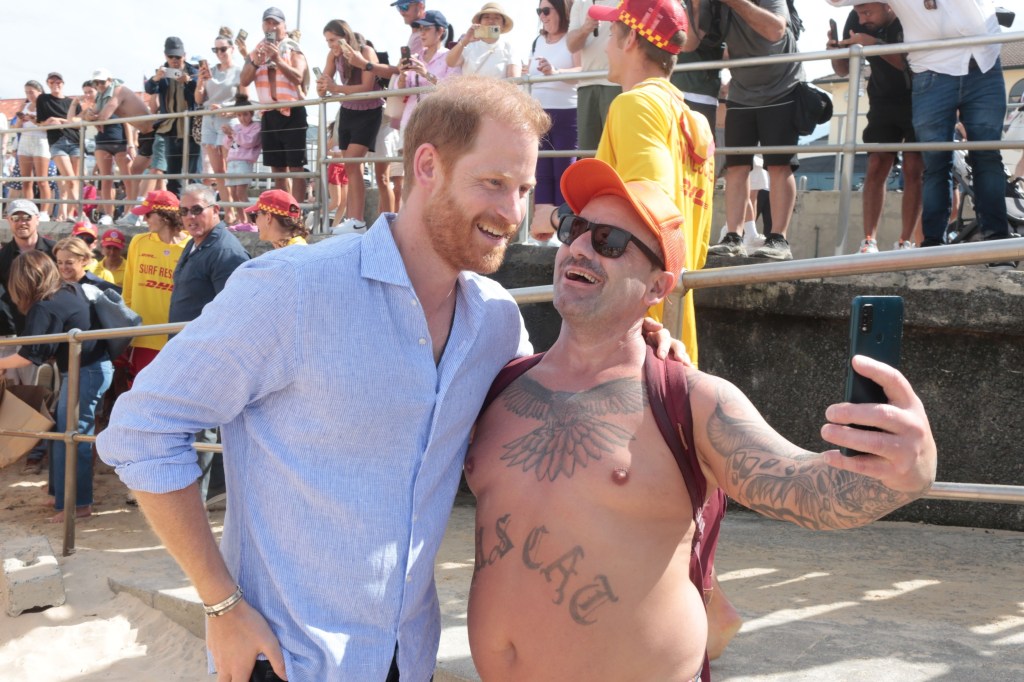 Prince Harry taking a selfie with a tattooed man at Bondi Beach.