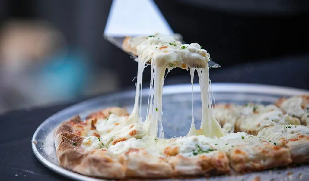 A slice of white pizza being lifted from a pan, showing long strings of melted cheese.