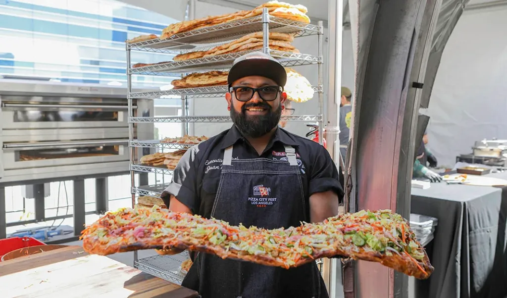 Chef Juan Torres of Triple R Cafe holding a long rectangular pizza at Pizza City Fest.