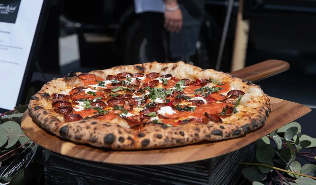 Pizza with pepperoni, red sauce, white cheese, and basil leaves on a wooden paddle.