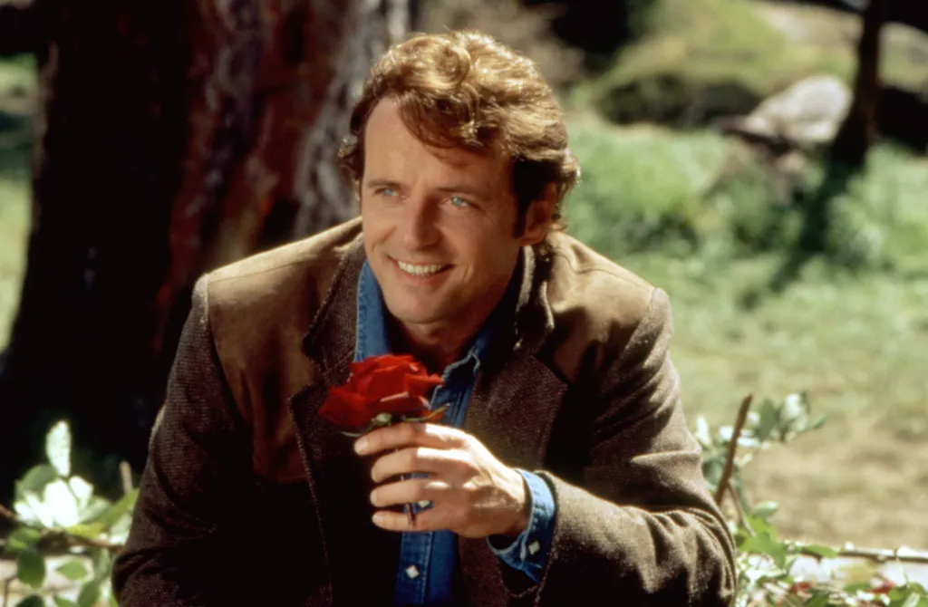 Aidan Quinn as Quinn in the 1998 movie "Practical Magic", holding a red rose and smiling.