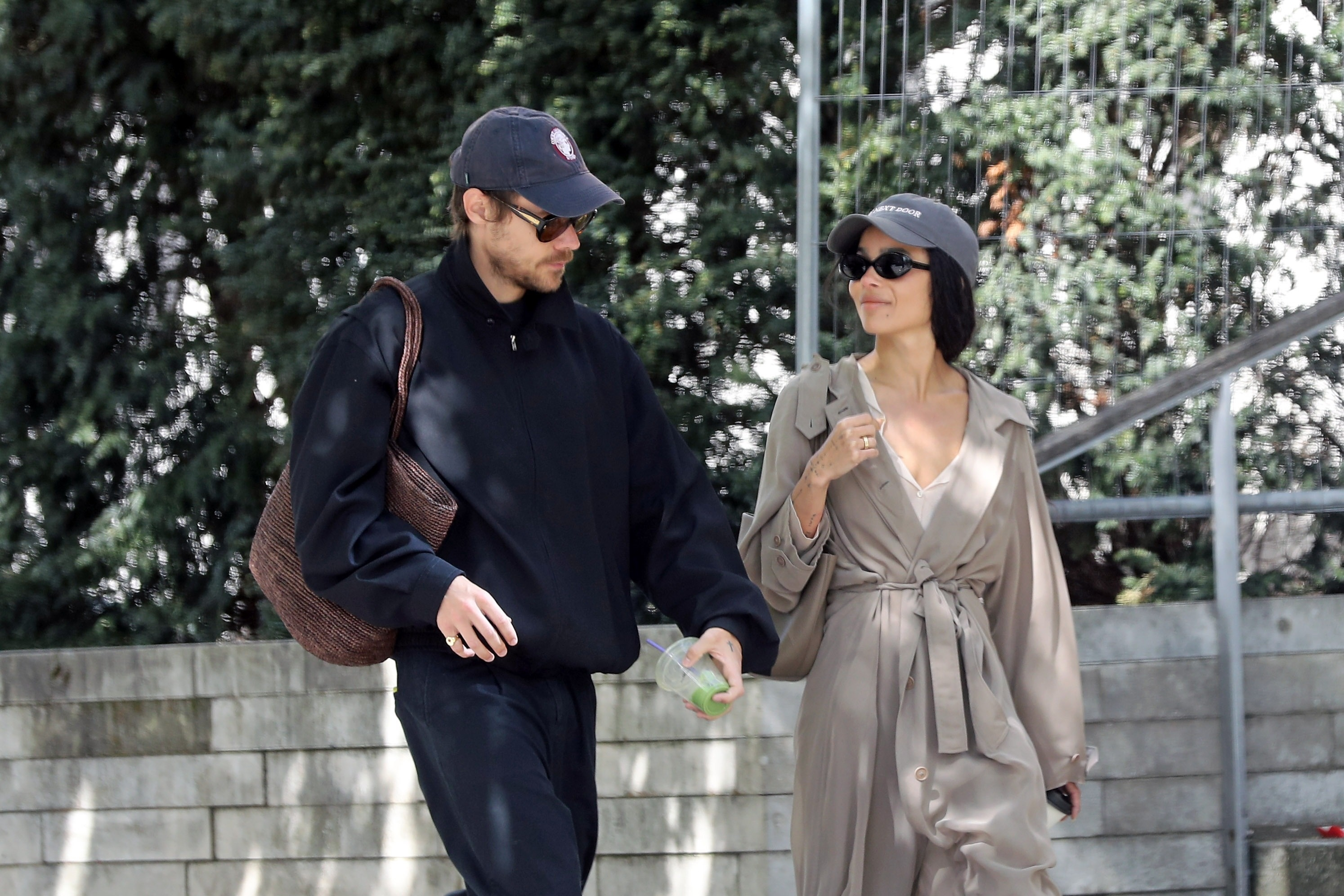 Harry Styles and Zoe Kravitz walking, with Harry holding a green drink and Zoe in a trench coat.