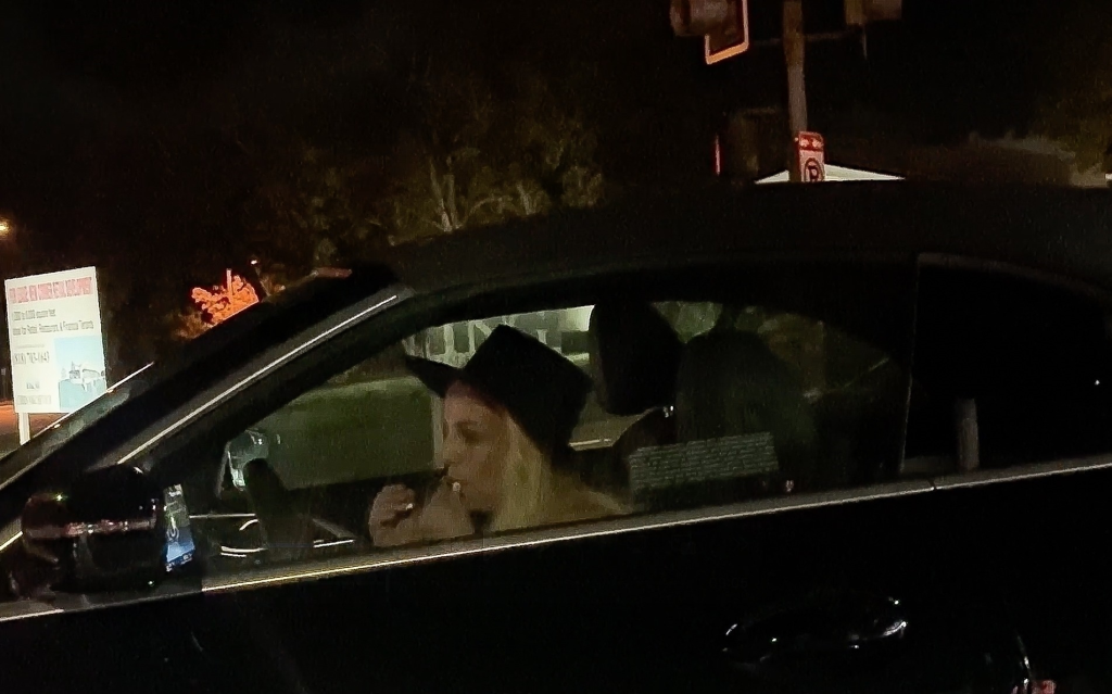 Britney Spears in a black convertible BMW at night, possibly smoking, with the window down.